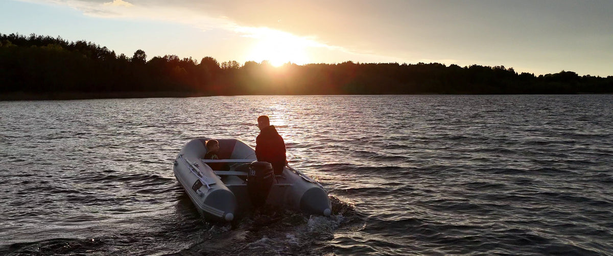 Adult and child in a grey ARGO DRIVE inflatable boat with an outboard motor on a lake at sunset