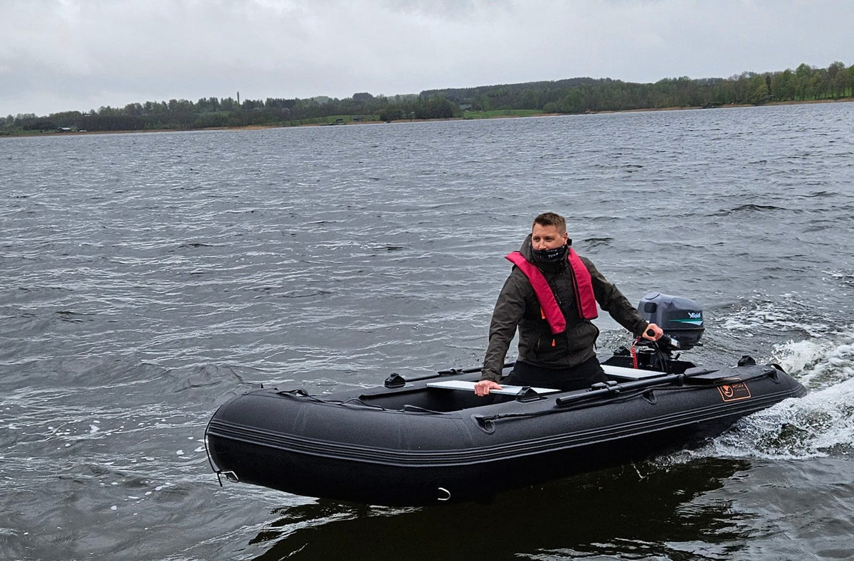 Man in a life jacket driving a black ARGO DRIVE inflatable boat with an Aiqidi electric outboard motor on a lake